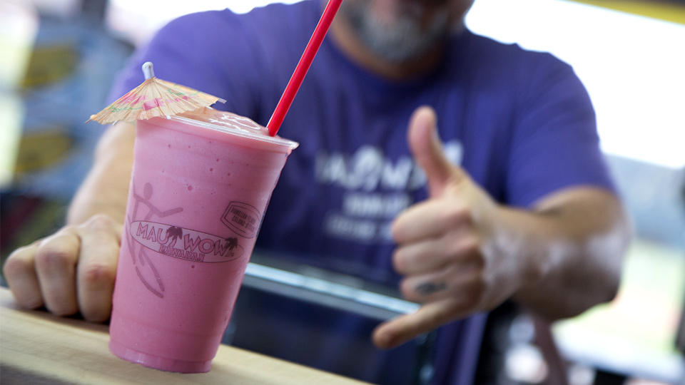 Maui Wowi franchisee makes cool surfer dude gesture while serving a purple smoothie.